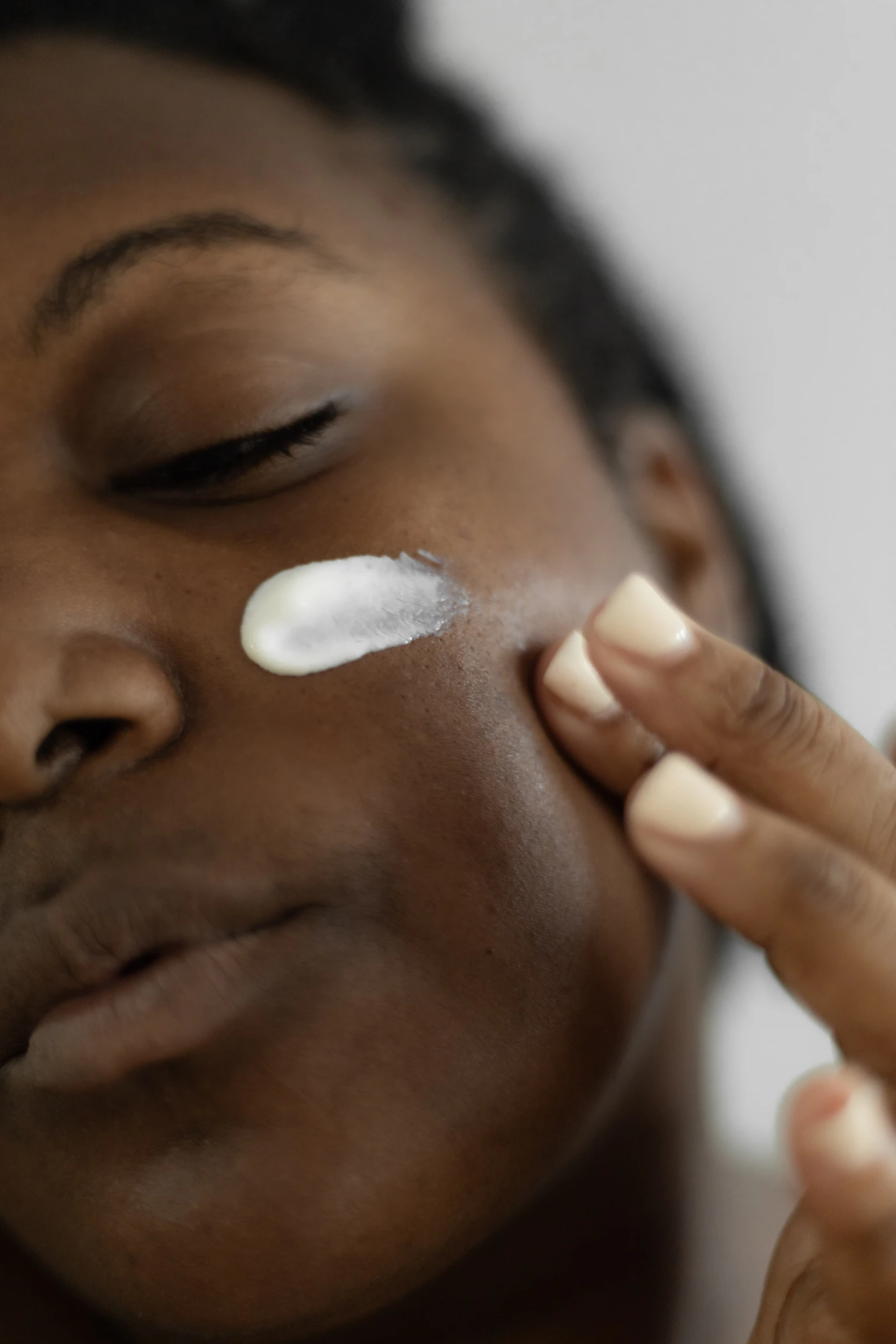 Woman applying moisturizer to her face, representing the sealed-in comfort a Deep Hydration Facial aims to leave skin with