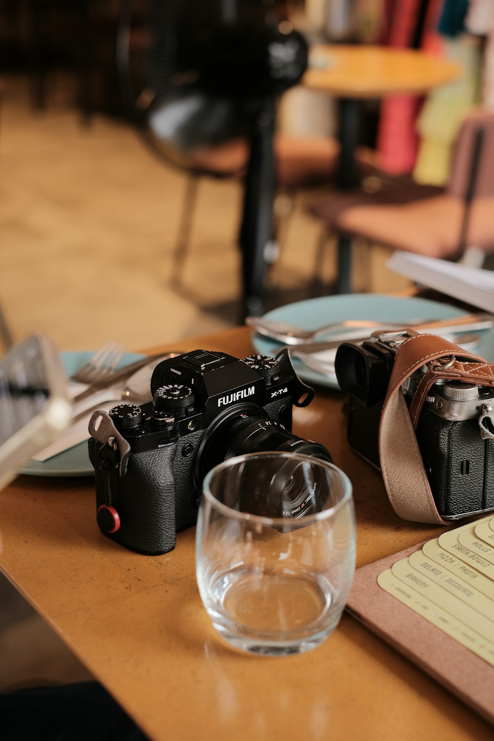 a table topped with a glass of water and two cameras