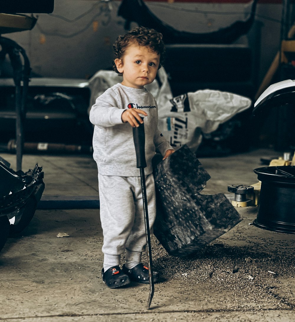 a little boy holding a broom and standing next to a pile of garbage