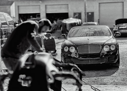 A sleek black luxury car being carefully detailed outdoors by a professional in a clean, minimal setting.