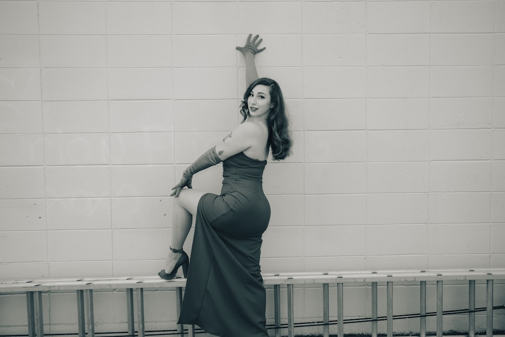 a woman in a long dress leaning against a wall