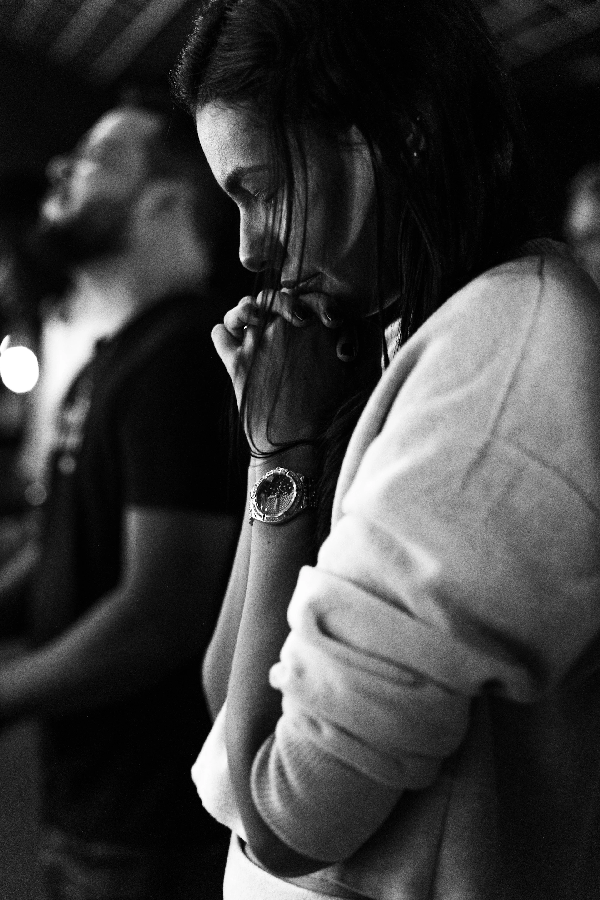 Woman with clasped hands, looking down in thought.