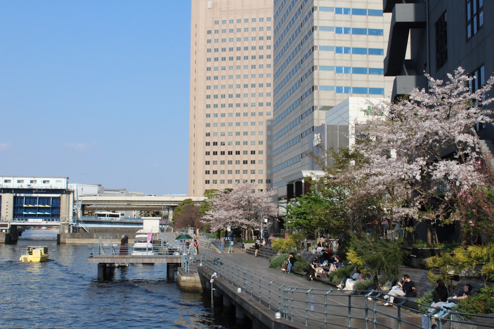 people sitting on the edge of a river next to tall buildings