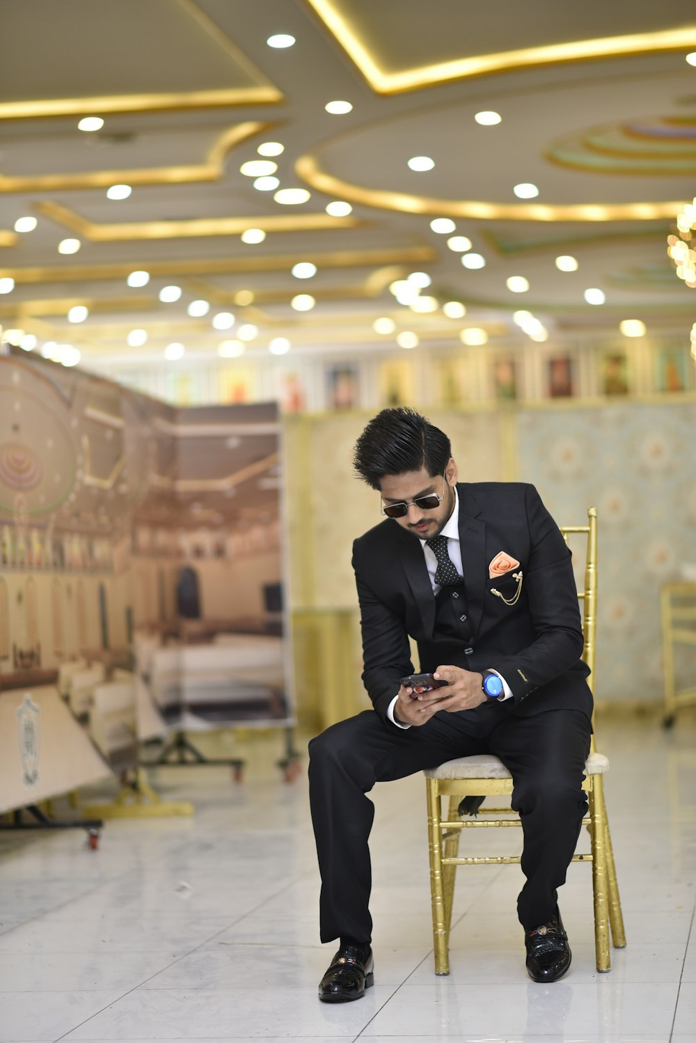 a man in a suit sitting on a chair looking at his cell phone