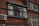 A brick building facade features several large windows with reflections of other structures. Numerous black cables and wires run horizontally across the exterior, accompanied by a wall-mounted air conditioning unit. The image conveys a sense of urban complexity and utility infrastructure.