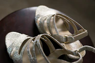 A pair of delicate golden sandals sparkling gently under warm lighting on a white surface.