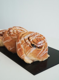 Close-up of a hand placing a fresh cinnamon roll into a paper bag on a wooden counter.