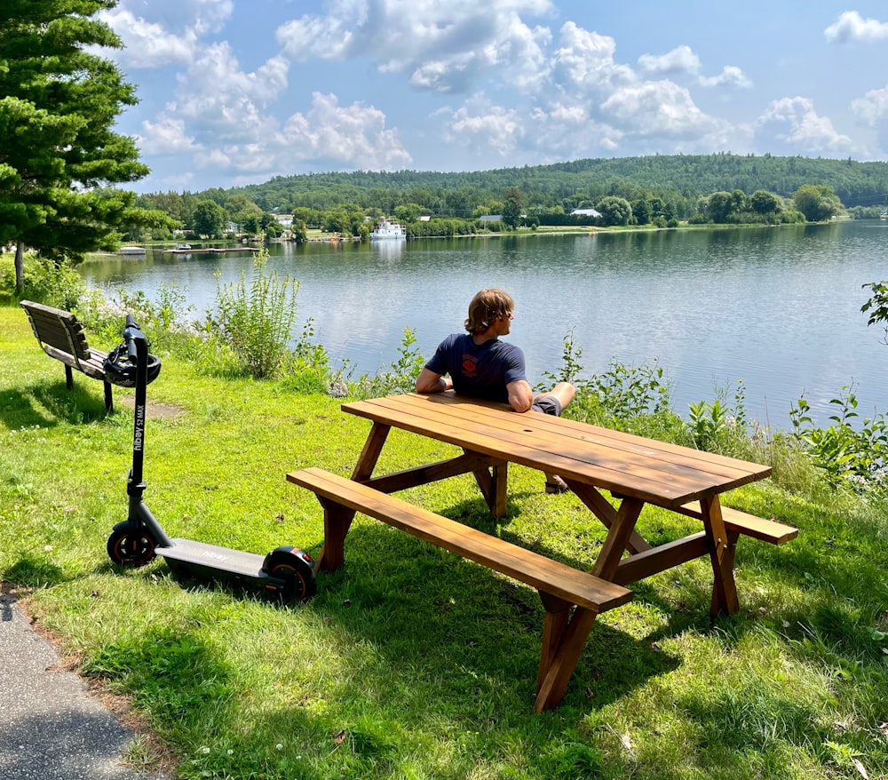 a young boy sitting at a picnic table next to a lake