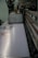A large industrial machine standing in a factory environment is captured up-close. The machine appears to be a printer or fabric printing device. The conveyor belt on the machine has a visible pattern, and there are various mechanical parts visible, showing its operational complexities.