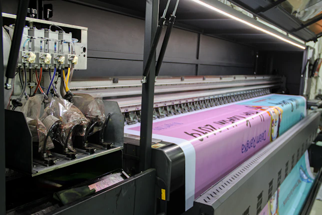 A large industrial printer feeding a long pink banner with printed text