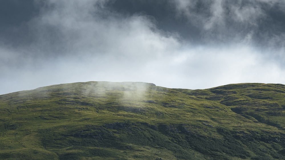 a grassy hill with clouds in the sky