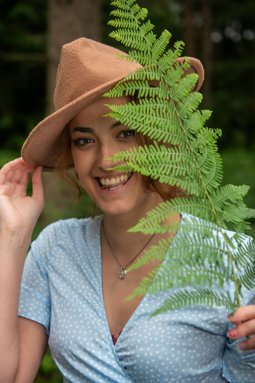 a woman with a hat is holding a fern