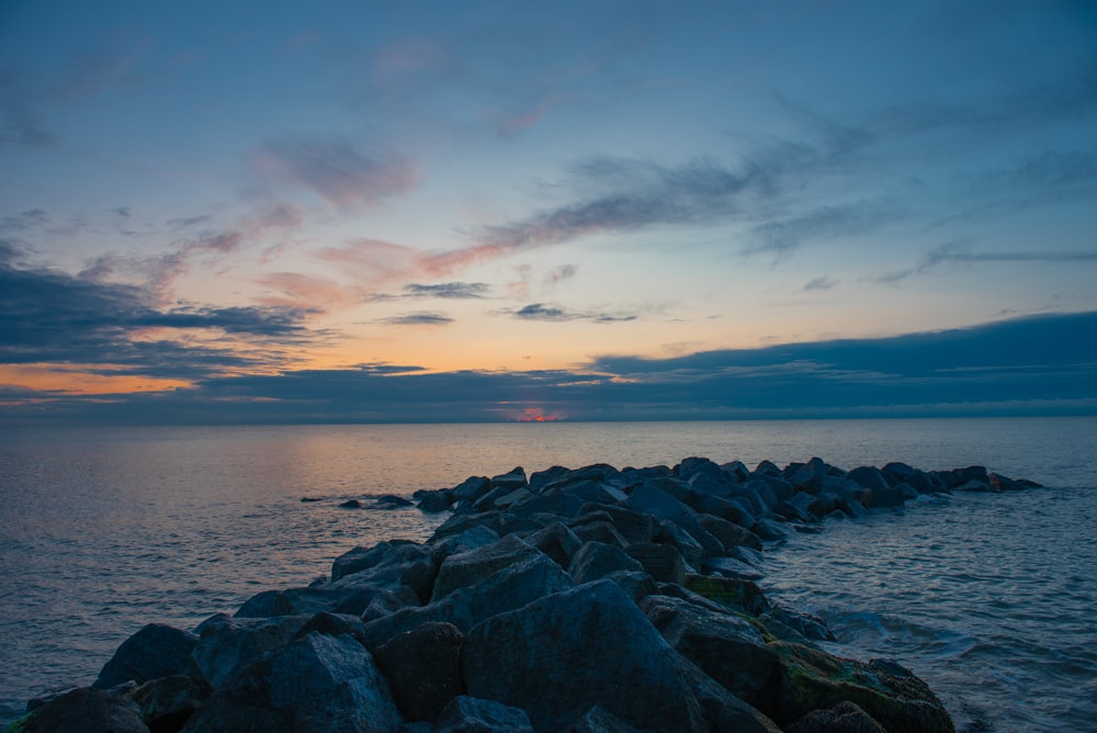 the sun is setting over the ocean and rocks