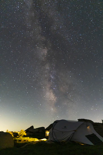A cozy sleeping bag laid out on a rocky campsite under a starry night sky.