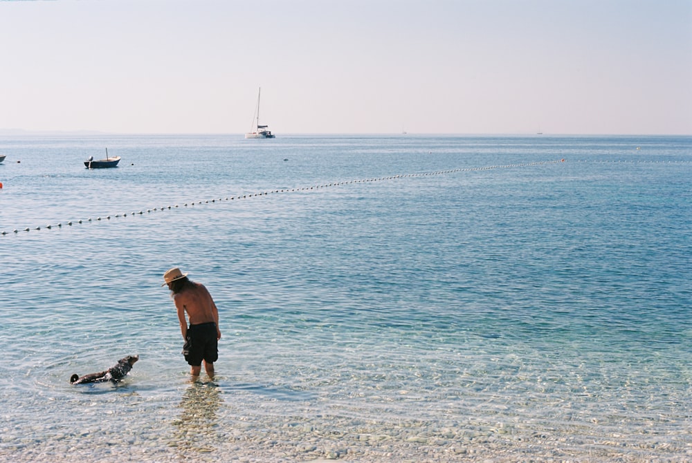 a man standing in the ocean with a dog