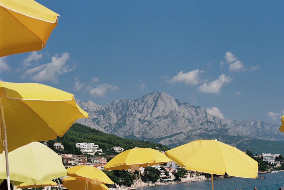 Gele parasols op de voorgrond, meer en rotsachtige berg op de achtergrond