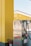 A brightly colored gas station featuring a yellow and black color scheme. Several metallic gas pumps are visible, with the text 'Hier tanken Sie PowerGas 60/40' printed on one of them. A fire extinguisher is placed nearby, and the modern architecture of the station is highlighted in the background.