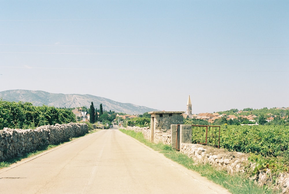 a dirt road with a stone wall and a clock tower in the distance