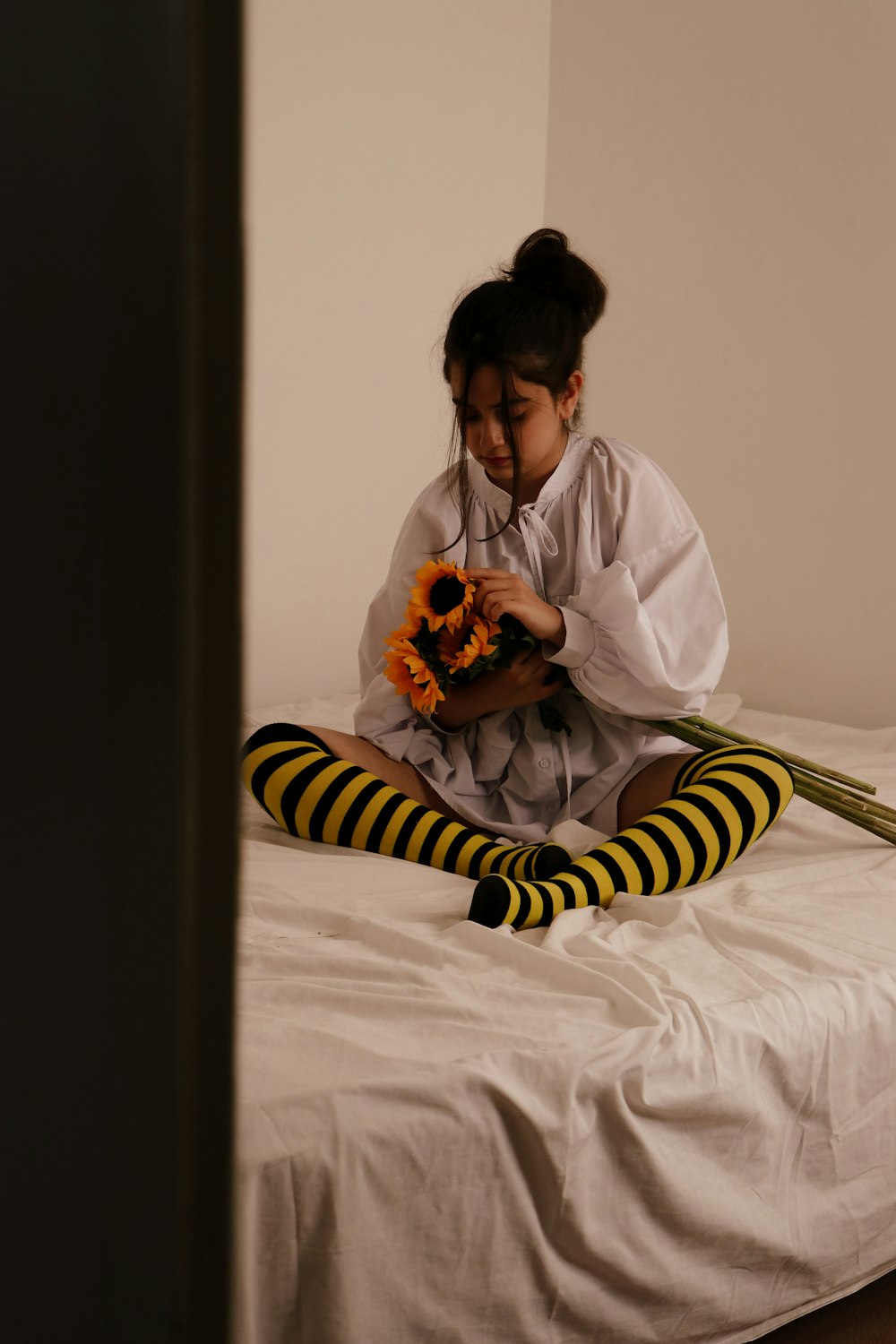 a girl sitting on a bed holding a sunflower