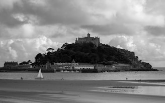 A dramatic black-and-white photo of an ancient castle perched on a rugged cliff under a moody sky.