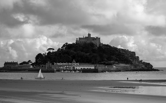 A dramatic black-and-white photo of an ancient castle perched on a rugged cliff under a moody sky.