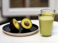 an avocado on a plate next to a glass of juice