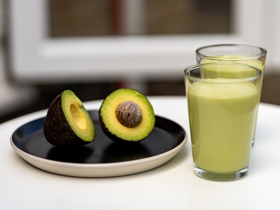 an avocado on a plate next to a glass of juice