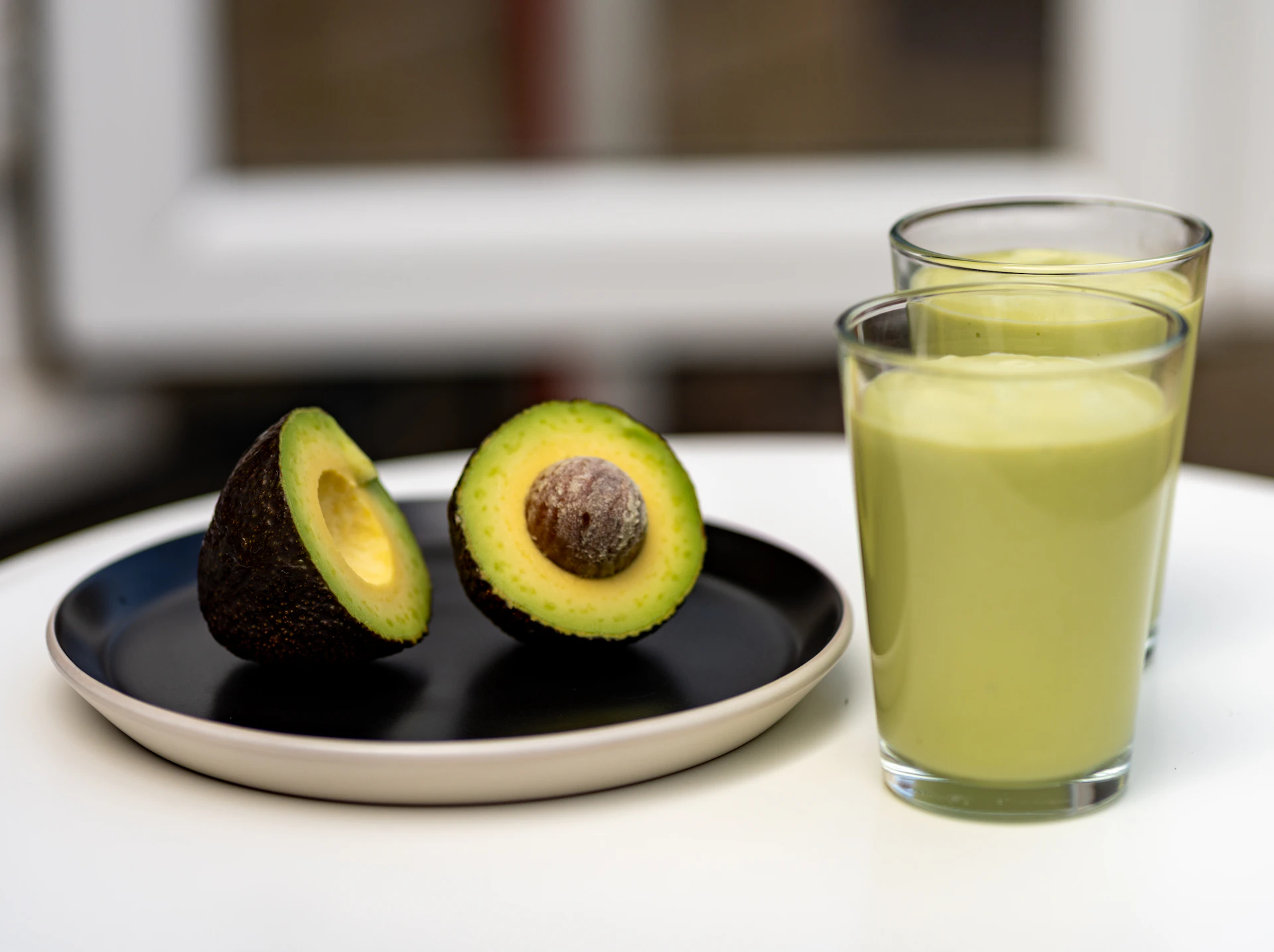 an avocado on a plate next to a glass of juice