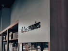 A modern retail store interior with a focus on minimalistic design. Shelves on the left side hold various boxed products, while a sleek, large sign reads 'Accessories' in bold letters. The lighting is soft, creating a calm ambiance.