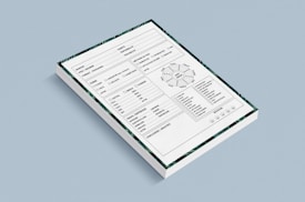 A stack of forms placed against a light blue background. Each form contains various sections including checkboxes, a circular diagram, tables, and lines for handwritten information. The forms also have a decorative border featuring green patterns.