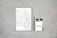 A document with checkboxes and text is placed on a flat, textured gray surface. Next to it, there is a black pencil, two black binder clips, and two small blank cards. The document appears to be some kind of form or template, featuring French text and various sections for input or selection.