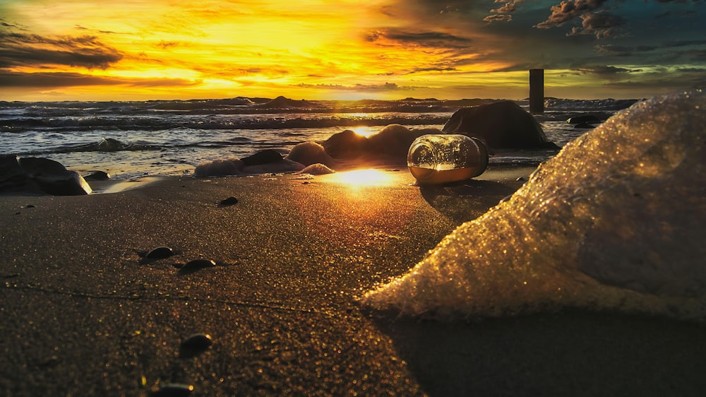 the sun is setting on a beach with rocks