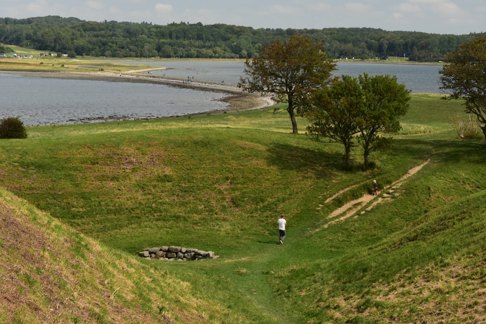 a person walking up a grassy hill next to a lake