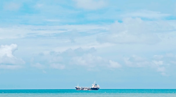 A serene blue-toned image of a modern ship navigating calm seas under a bright sky.