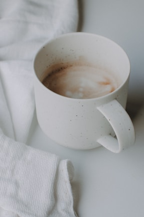 A minimalist white cup resting on a cozy knitted blanket near a window.