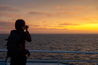 A travel influencer capturing a sunset moment on a remote coastline, blending natural beauty with a premium cinematic feel.