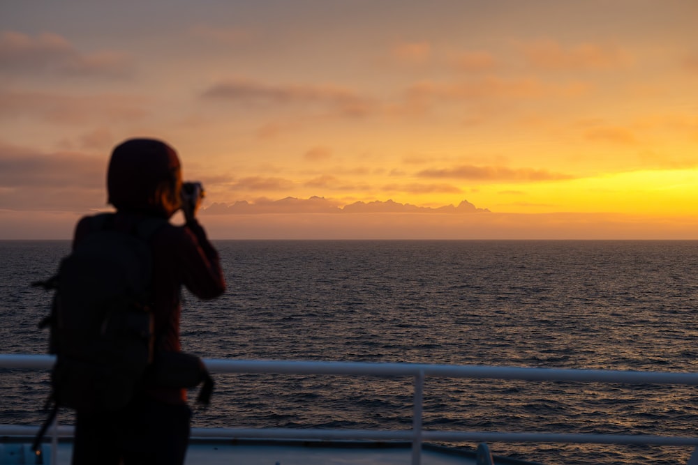 eine Person, die ein Foto von einem Sonnenuntergang auf einem Boot macht