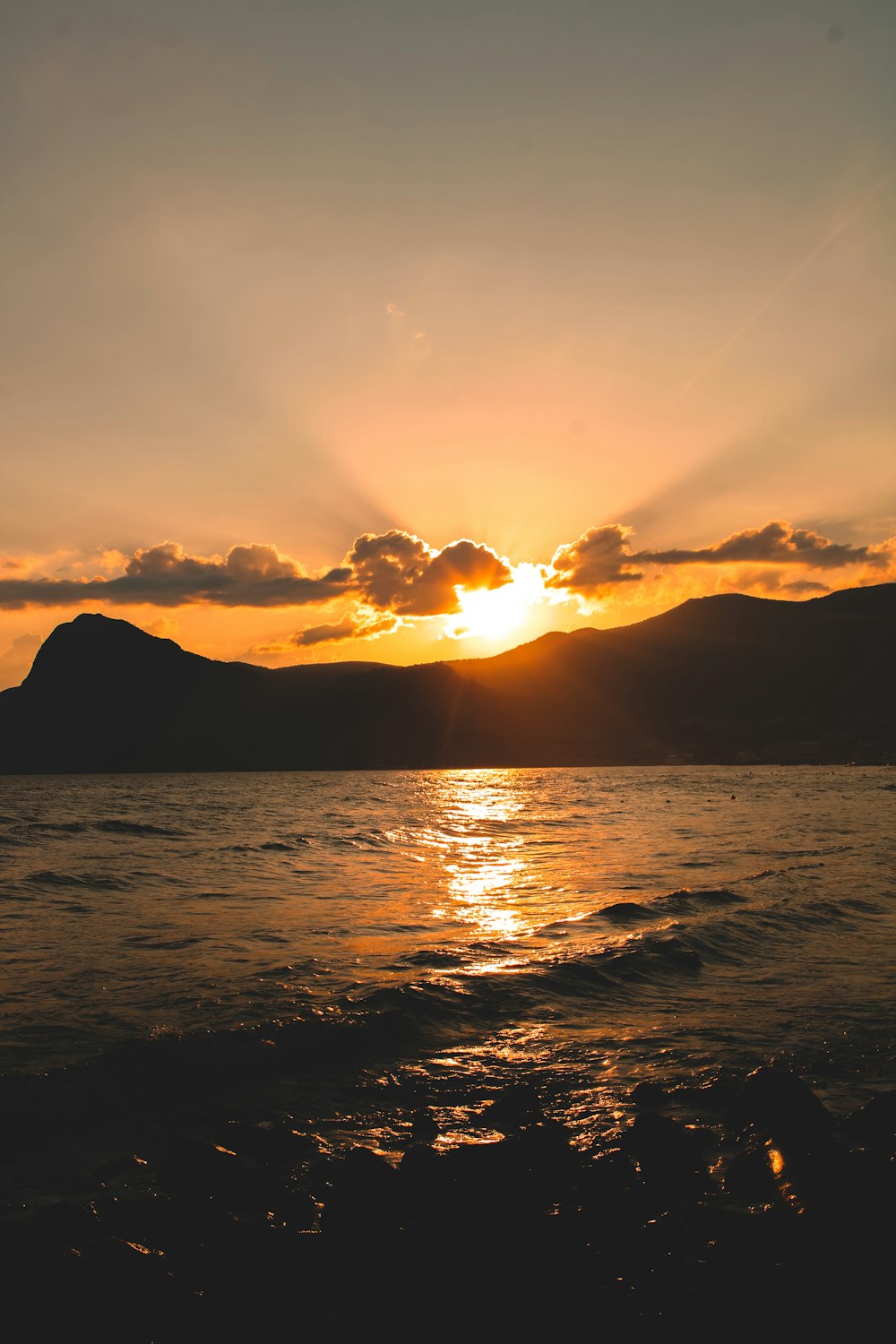 the sun is setting over the ocean with mountains in the background