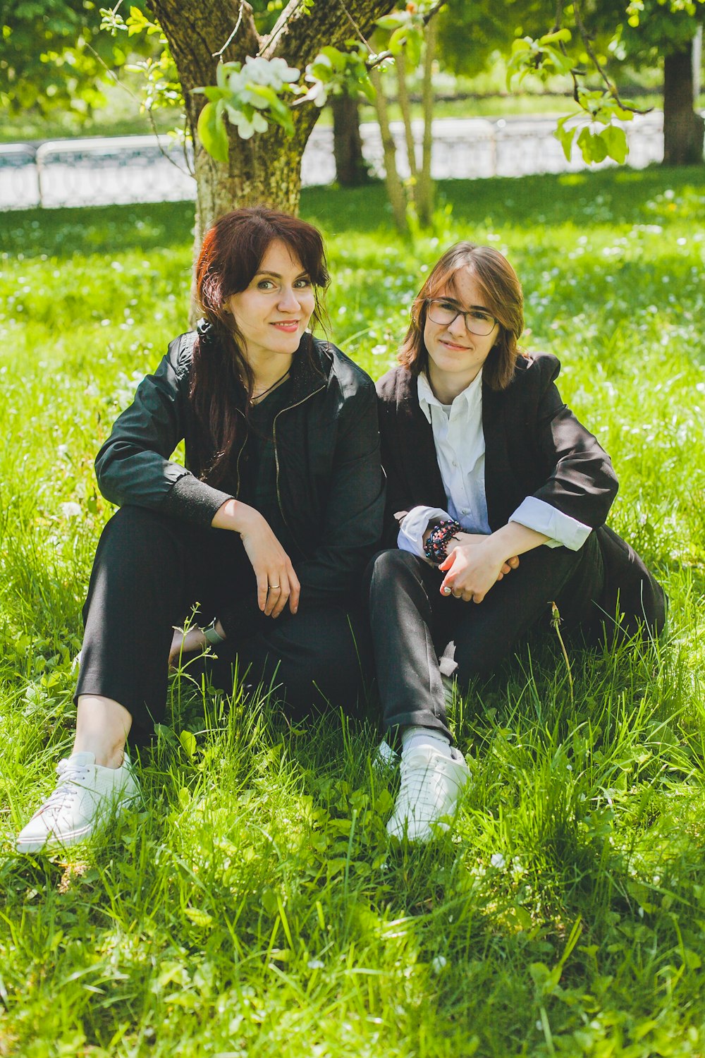 two women sitting in the grass under a tree
