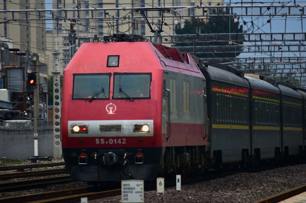 a red train traveling down train tracks next to a tall building