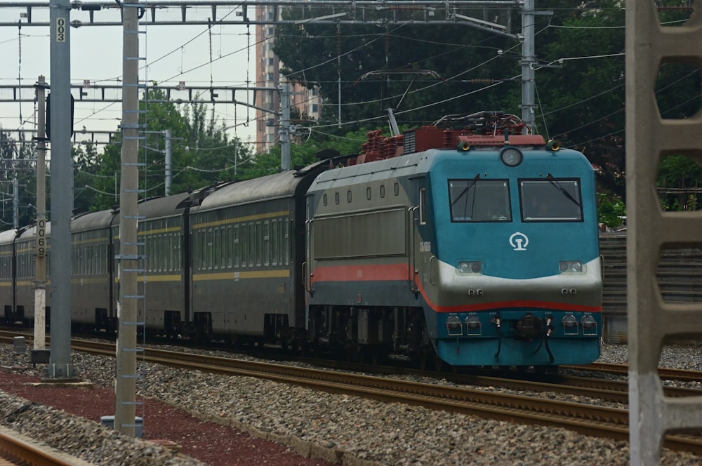 a blue train traveling down train tracks next to a forest