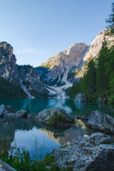 A serene mountain lake reflecting a deep blue sky at dawn, surrounded by lush green forests.