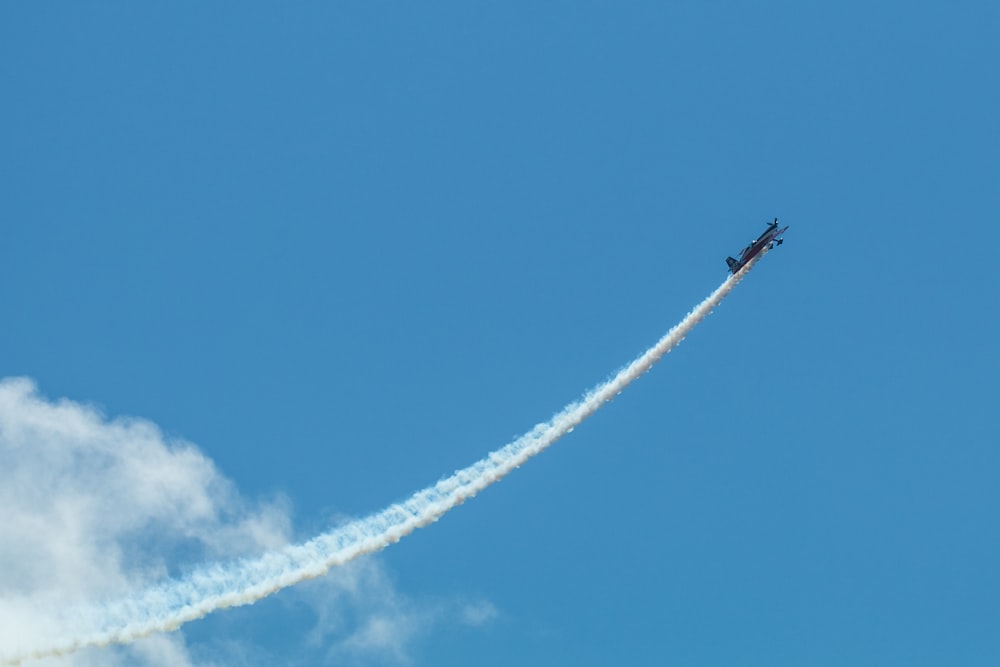 a plane flying in the sky leaving a trail of smoke behind it