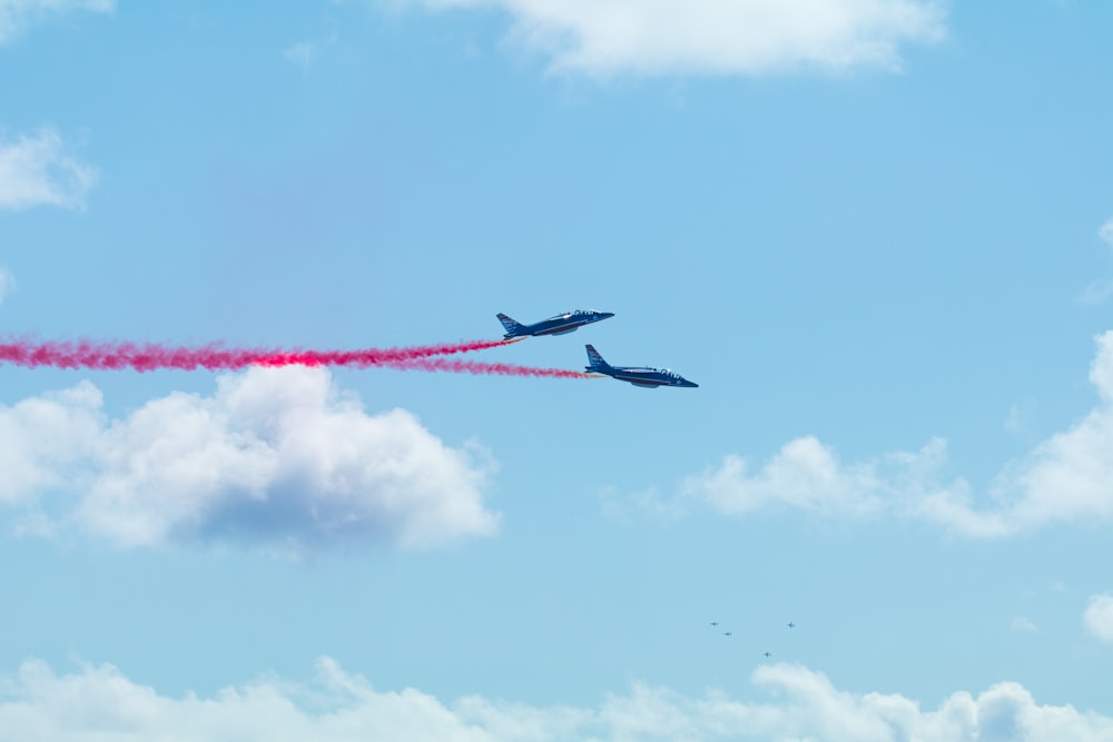 two airplanes flying in the sky with red smoke coming out of them