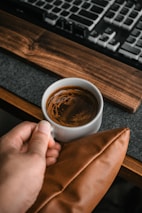 Hands holding a photogenic mug filled with coffee, resting on a casual home desk setup.