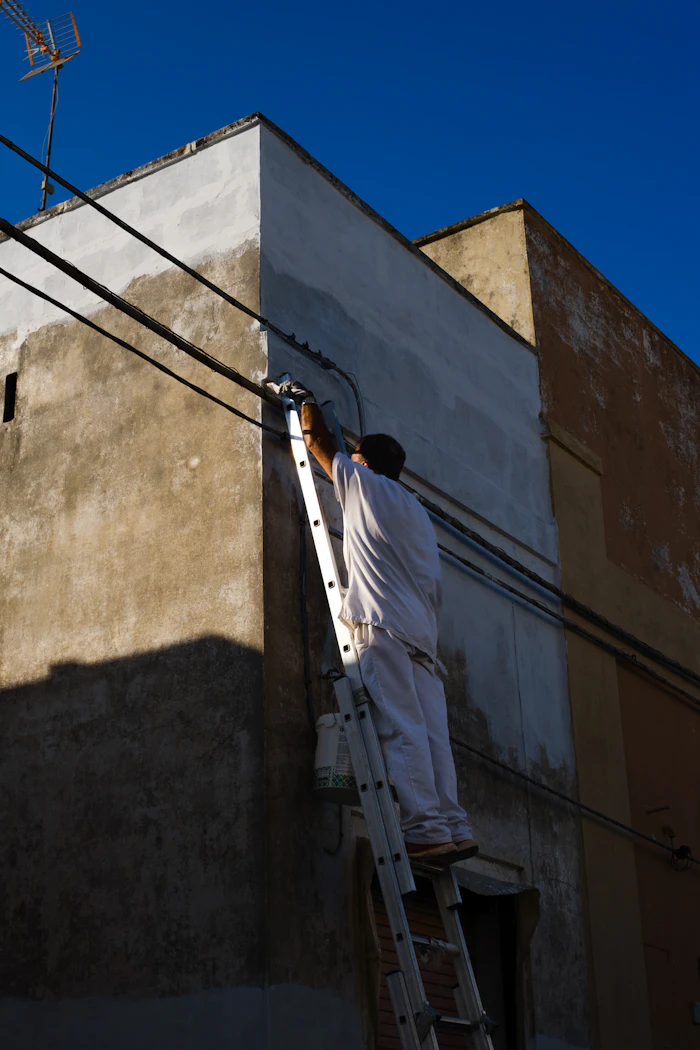 Pintor em escada pintando fachada externa de prédio