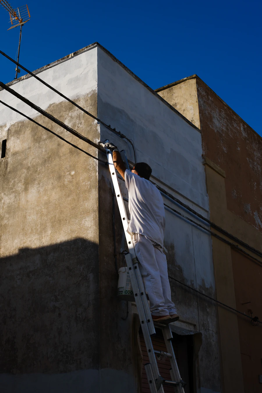 Pintor em escada pintando fachada externa de prédio