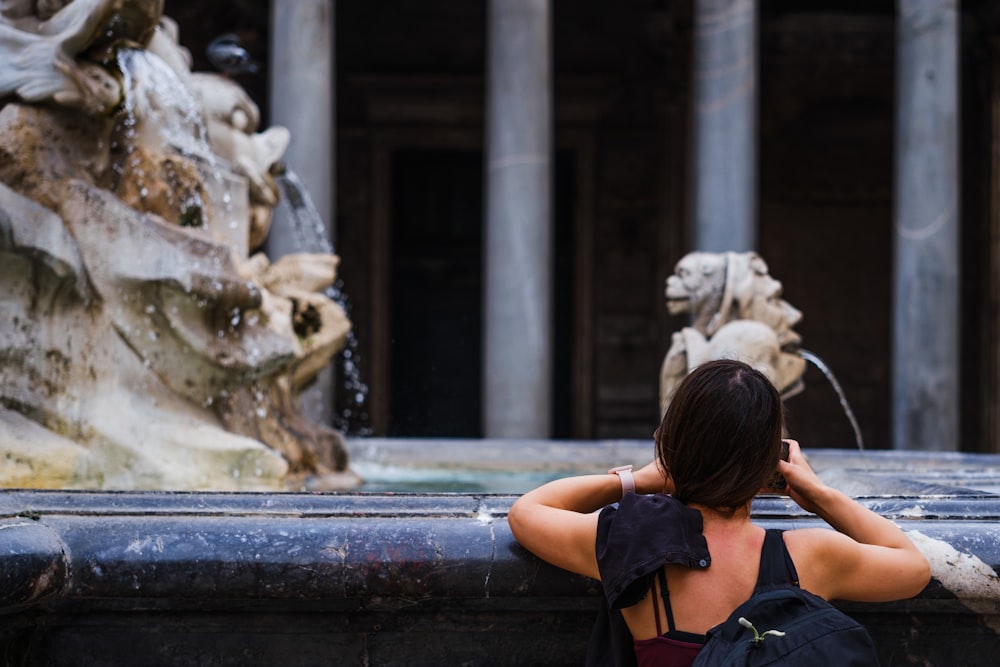 a woman leaning on a fountain looking at the water