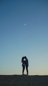 Silhouette of the couple embracing on a hilltop with a pastel sky behind them.