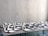 A table is covered with an arrangement of white ceramic dishes and cups of various shapes and sizes, set against a light gray textured wall.